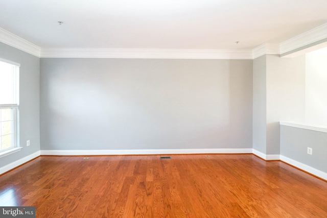 spare room with ornamental molding, visible vents, baseboards, and wood finished floors