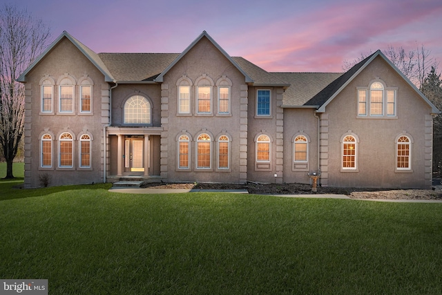 view of front of house with stucco siding, a lawn, and a shingled roof