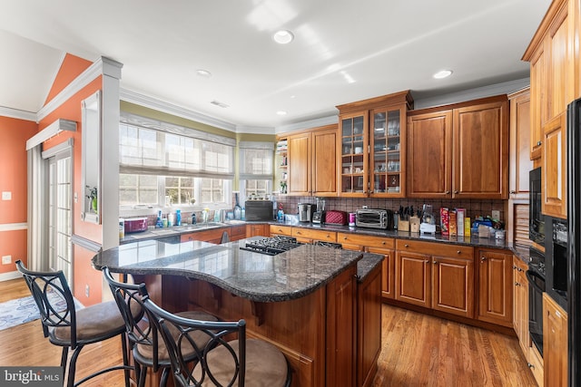 kitchen with glass insert cabinets, a kitchen bar, crown molding, light wood-type flooring, and backsplash