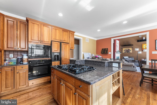 kitchen with light wood finished floors, visible vents, backsplash, a center island, and black appliances