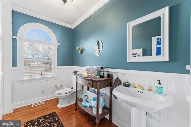 bathroom with wood finished floors, visible vents, a wainscoted wall, ornamental molding, and toilet