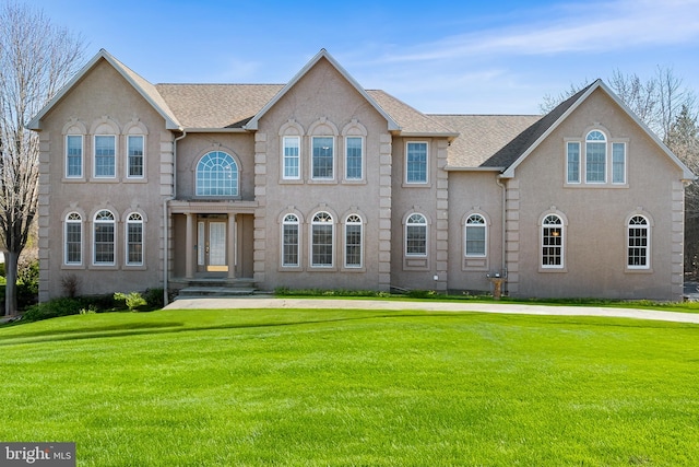 colonial inspired home with stucco siding, roof with shingles, and a front lawn