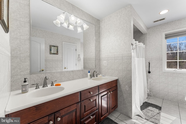 full bathroom with tile walls, double vanity, visible vents, and a sink