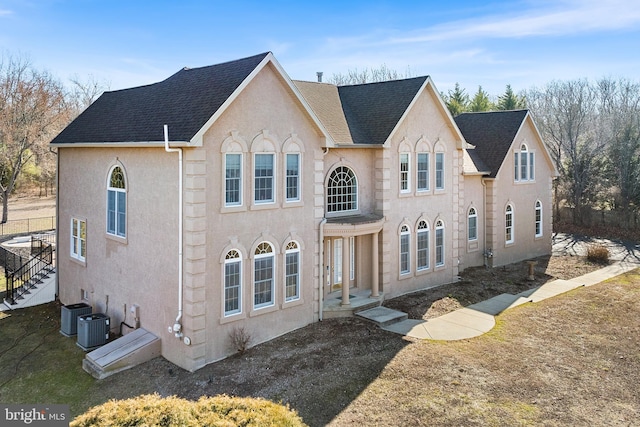 view of front of home with central air condition unit, stucco siding, and roof with shingles