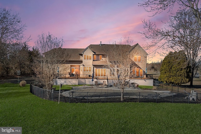 back of property at dusk with a patio area, a yard, and fence