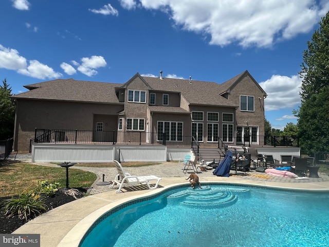 back of property with an outdoor pool, stucco siding, a patio, and a wooden deck