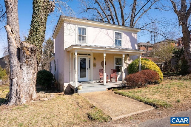 view of front of house featuring stucco siding, a standing seam roof, a porch, a front yard, and metal roof