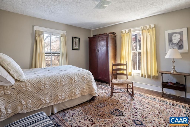 bedroom with a textured ceiling, baseboards, and wood finished floors