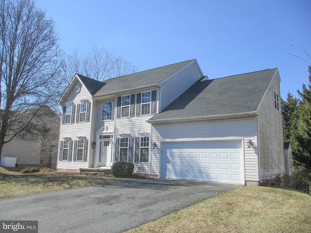 colonial inspired home with driveway, an attached garage, roof with shingles, and a front yard