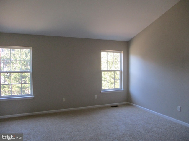 carpeted spare room featuring lofted ceiling, plenty of natural light, visible vents, and baseboards