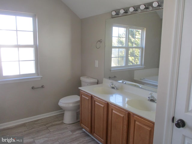 bathroom featuring vaulted ceiling, double vanity, a sink, and toilet