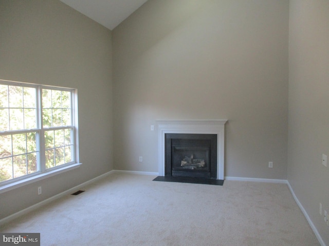 unfurnished living room featuring carpet floors, a fireplace with flush hearth, visible vents, and baseboards