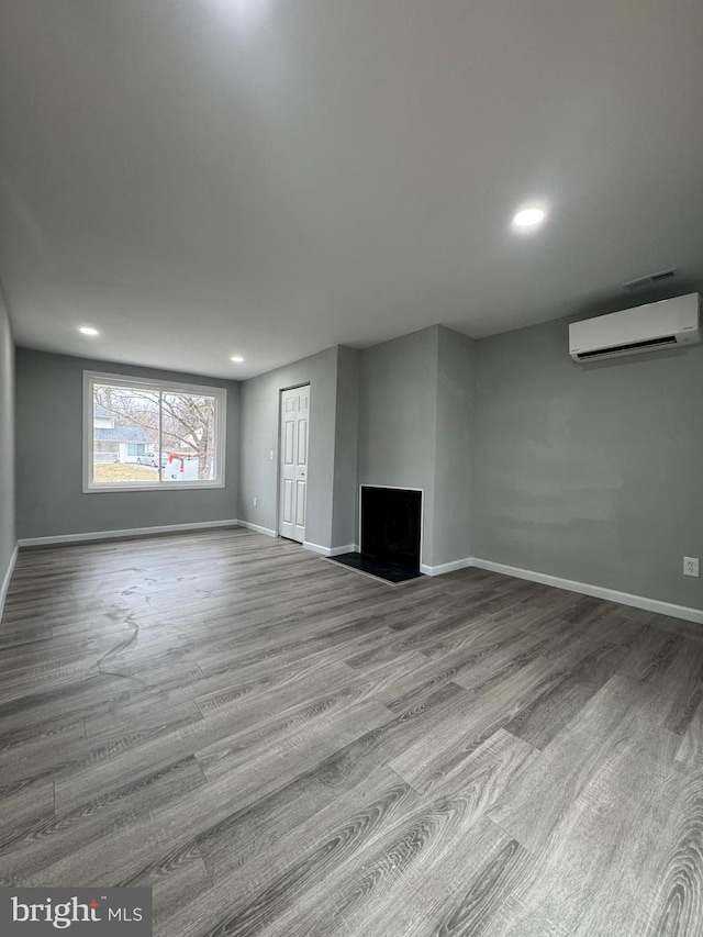 unfurnished living room featuring a wall mounted air conditioner, baseboards, wood finished floors, and recessed lighting