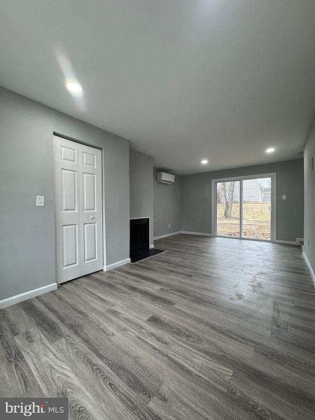 unfurnished living room with recessed lighting, an AC wall unit, baseboards, and wood finished floors