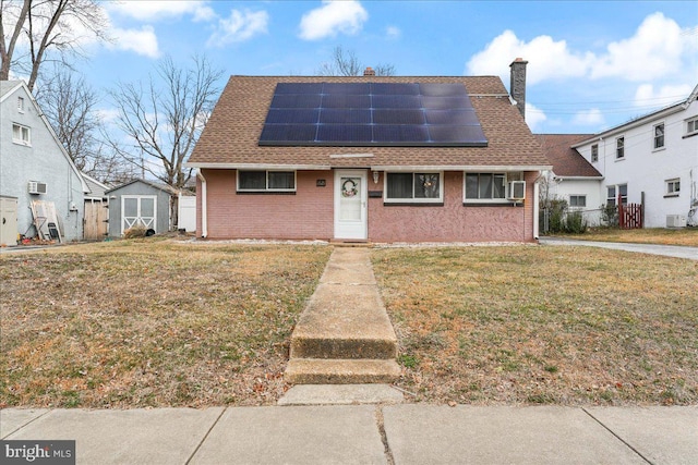 view of front of house with brick siding, roof with shingles, a chimney, solar panels, and a front yard