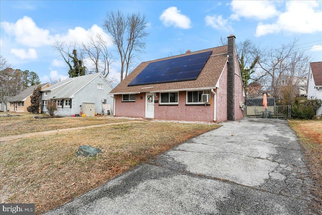 view of front of property featuring a front yard, a chimney, roof with shingles, roof mounted solar panels, and brick siding