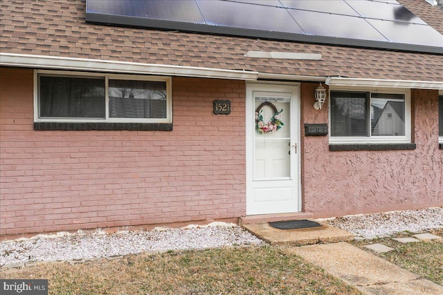 entrance to property featuring roof with shingles, brick siding, and stucco siding