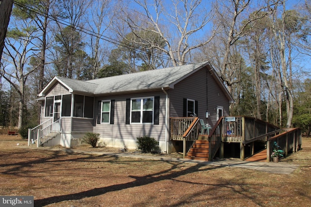 view of side of home featuring a wooden deck, roof with shingles, stairs, and a sunroom