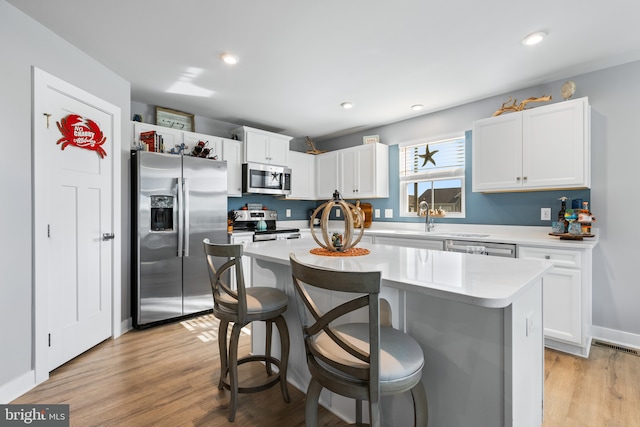 kitchen with appliances with stainless steel finishes, a center island, light countertops, and light wood-style flooring