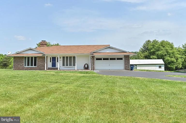 ranch-style home with brick siding, a chimney, a garage, driveway, and a front lawn