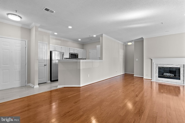 unfurnished living room with a textured ceiling, a premium fireplace, visible vents, light wood finished floors, and crown molding