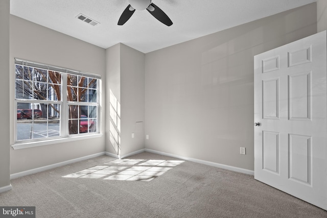 carpeted spare room featuring a textured ceiling, a ceiling fan, visible vents, and baseboards