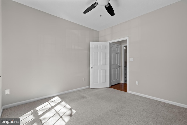 empty room featuring vaulted ceiling, carpet floors, a ceiling fan, and baseboards