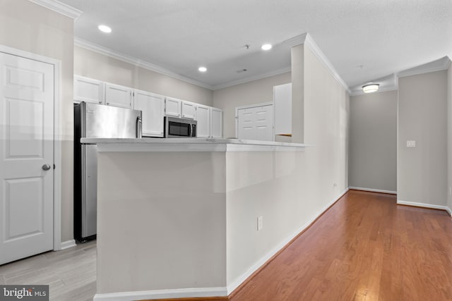 kitchen with crown molding, stainless steel appliances, white cabinets, and light wood-style floors