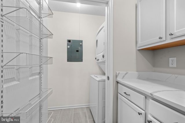 clothes washing area featuring laundry area, electric panel, baseboards, stacked washer / dryer, and a textured ceiling