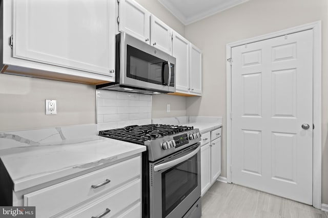 kitchen featuring white cabinets, ornamental molding, appliances with stainless steel finishes, light stone countertops, and tasteful backsplash