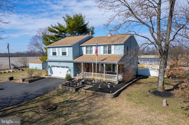 traditional home featuring fence, aphalt driveway, a front yard, covered porch, and an attached garage