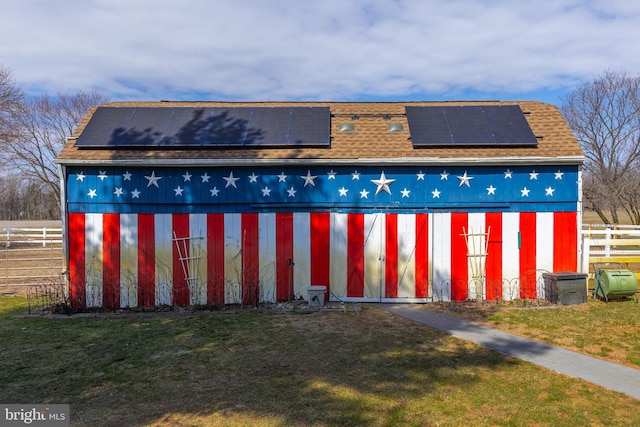 exterior space featuring a shingled roof, fence, roof mounted solar panels, a lawn, and an outdoor structure