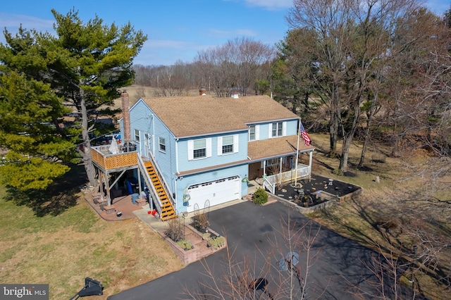 view of front of home featuring an attached garage, a shingled roof, stairway, a front yard, and driveway