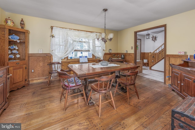 dining room with hardwood / wood-style flooring, stairway, a wainscoted wall, and a chandelier