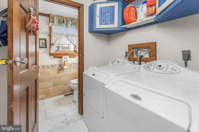 laundry area featuring a wainscoted wall, washing machine and clothes dryer, laundry area, tile walls, and marble finish floor