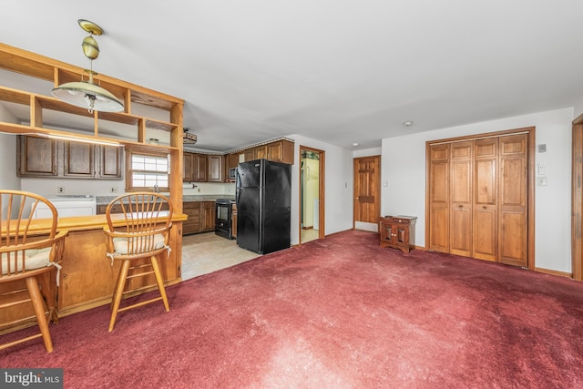 kitchen featuring light colored carpet, black appliances, brown cabinets, and baseboards