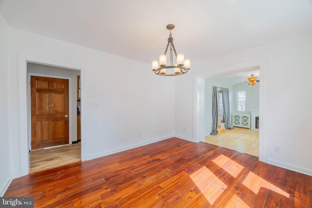 empty room featuring a notable chandelier, hardwood / wood-style flooring, and baseboards