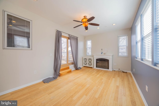 unfurnished living room with recessed lighting, wood finished floors, a ceiling fan, baseboards, and a glass covered fireplace