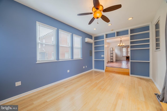 spare room featuring baseboards, wood finished floors, a wall mounted air conditioner, ceiling fan with notable chandelier, and recessed lighting