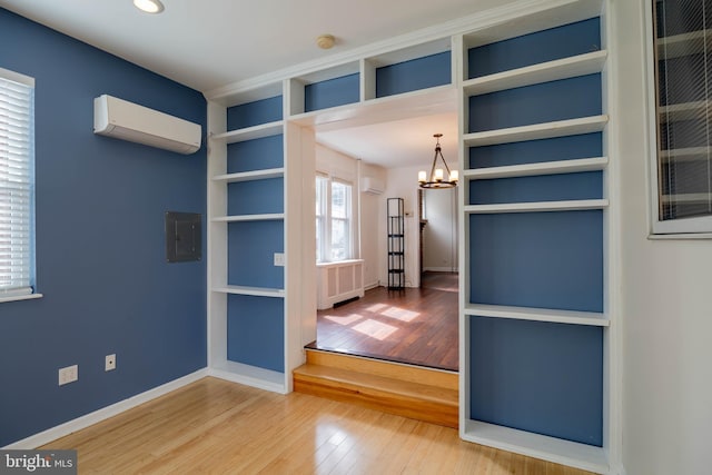 empty room featuring hardwood / wood-style flooring, a notable chandelier, an AC wall unit, electric panel, and radiator heating unit