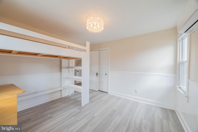 unfurnished bedroom with a wainscoted wall, a wall unit AC, wood finished floors, and a notable chandelier