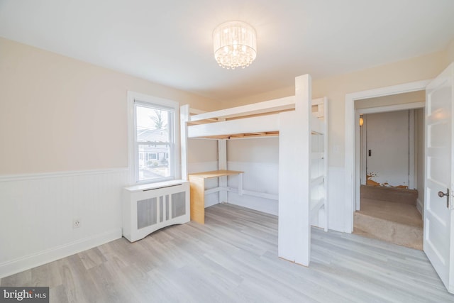 unfurnished bedroom with wainscoting, radiator heating unit, wood finished floors, a notable chandelier, and a closet