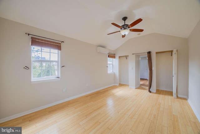 unfurnished bedroom with vaulted ceiling, light wood-type flooring, a wall unit AC, and baseboards