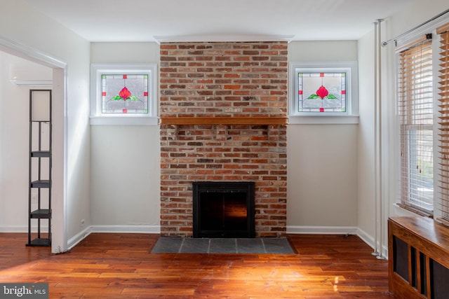 unfurnished living room with a healthy amount of sunlight, a fireplace, baseboards, and wood finished floors