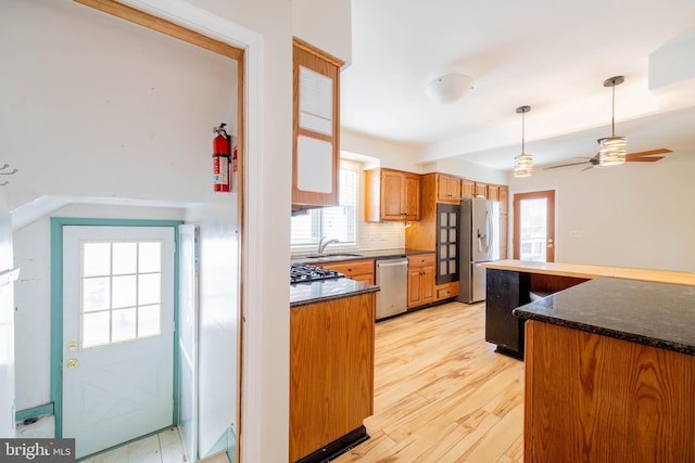 kitchen with decorative light fixtures, light wood finished floors, backsplash, appliances with stainless steel finishes, and a sink