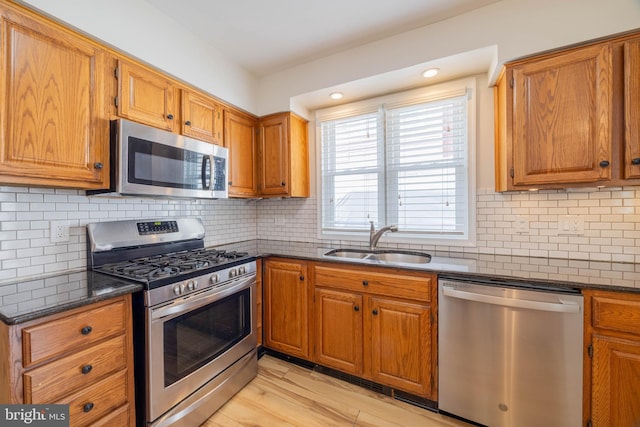 kitchen featuring tasteful backsplash, brown cabinetry, dark stone counters, stainless steel appliances, and a sink