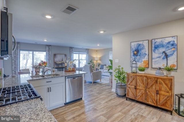 kitchen featuring a sink, visible vents, open floor plan, light wood-type flooring, and dishwasher