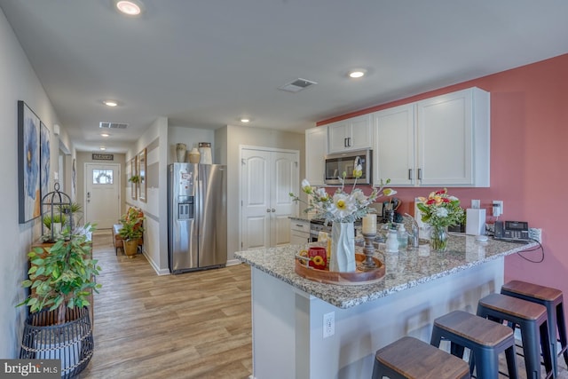 kitchen featuring a peninsula, appliances with stainless steel finishes, visible vents, and light stone counters