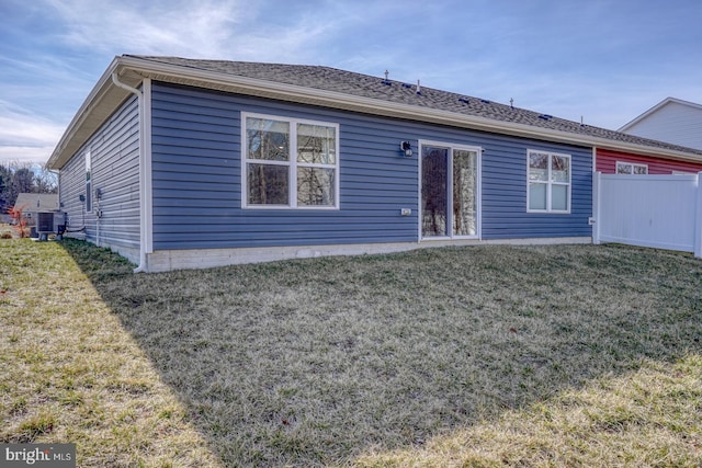 back of property featuring a shingled roof, a lawn, fence, and central AC unit