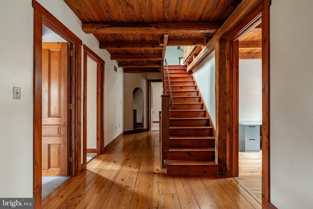 hall with arched walkways, wooden ceiling, hardwood / wood-style flooring, beamed ceiling, and stairs